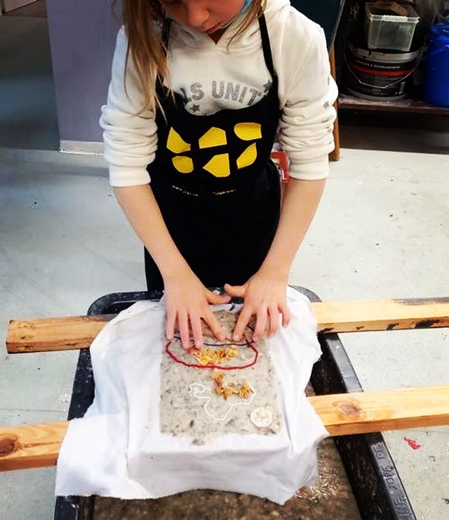 Mädchen mit Schürze arbeitet an einem Blatt selbstgeschöpftem Papier