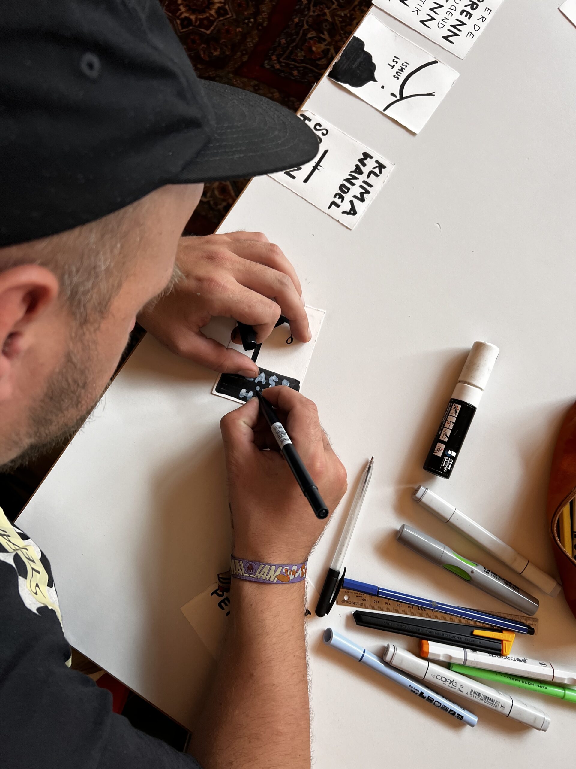 Junger Mann von oben fotografiert, zeichnet mit schwarzen Stift an einem Mini-Plakat